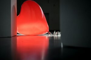 A glowing red heart-shaped balloon rests on the floor casting a warm light in an indoor setting.